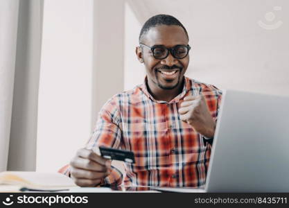 Afro guy gets profit. Happy african american man is buying or ordering online with pc. Businessman has transaction using credit card from home. Ecommerce and consumerism concept. Internet banking.. Afro guy gets profit. Man is buying or ordering online. Ecommerce and consumerism concept.