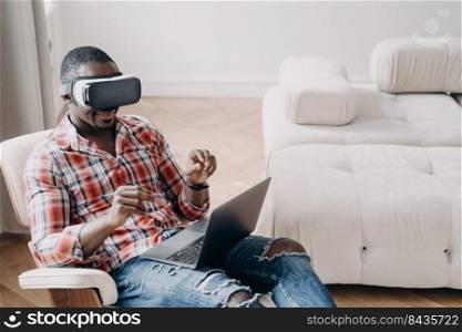 Afro man in vr headset. Workplace at home office. Businessman has virtual meeting. Relaxed freelancer is sitting in chair and working on project. High tech digital technology and vr gaming.. Afro man in vr headset at home office. Relaxed freelancer sitting in chair and working on project.