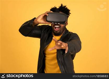 Afro man playing video games with VR glasses while standing over an isolated background. Technology concept.