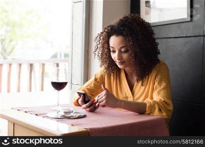 Afro woman typing on smartphone in restaurant
