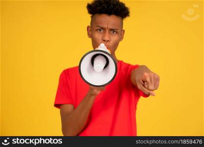 Afro young man screaming to someone with a megaphone while pointing to the camera.