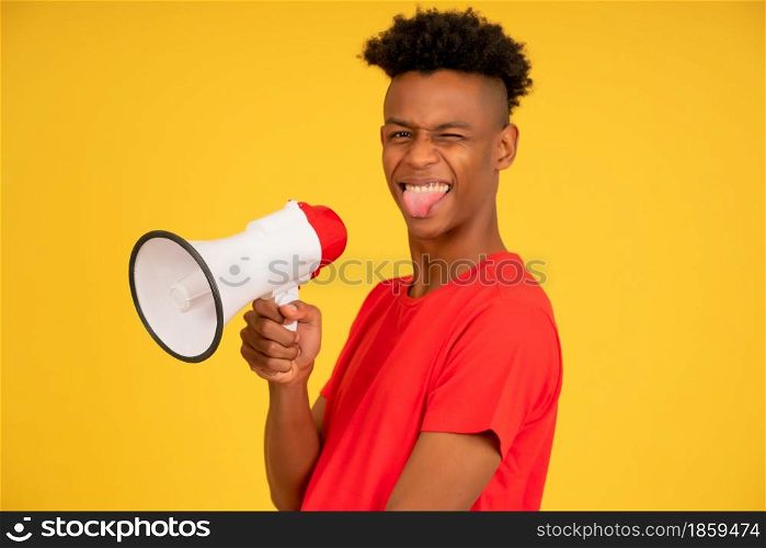 Afro young man using a megaphone to raise his voice while standing against a yellow background. Advertising and promotion concept.