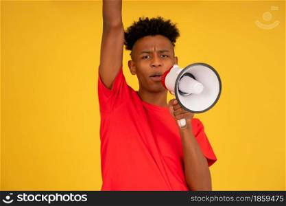 Afro young man using a megaphone to raise his voice while standing against a yellow background. Advertising and promotion concept.