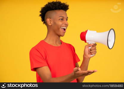 Afro young man using a megaphone to raise his voice while standing against a yellow background. Advertising and promotion concept.