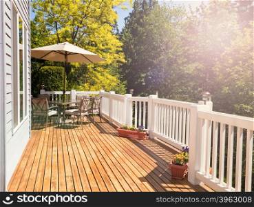 Afternoon bright daylight on outdoor home cedar deck with furniture and open umbrella. Light effect applied to image. Horizontal layout.