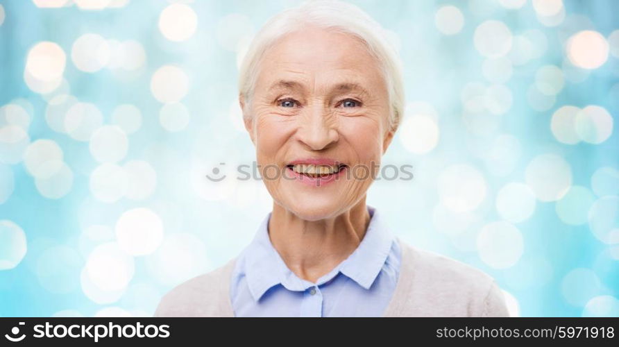 age and people concept - happy smiling senior woman face over blue holidays lights background. happy senior woman face over blue lights