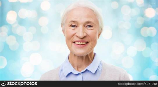 age and people concept - happy smiling senior woman face over blue holidays lights background. happy senior woman face over blue lights
