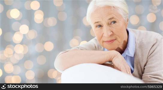 age and people concept - happy smiling senior woman face over holidays lights background. happy senior woman resting on sofa over lights