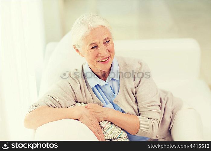age and people concept - happy smiling senior woman sitting on sofa at home. happy senior woman face at home