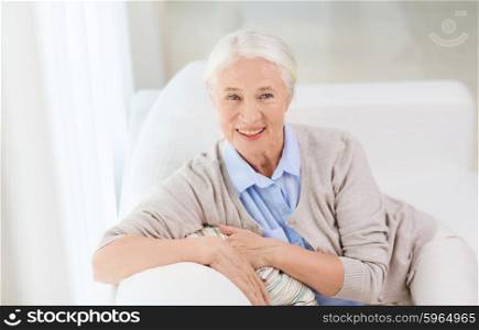 age and people concept - happy smiling senior woman sitting on sofa at home. happy senior woman face at home