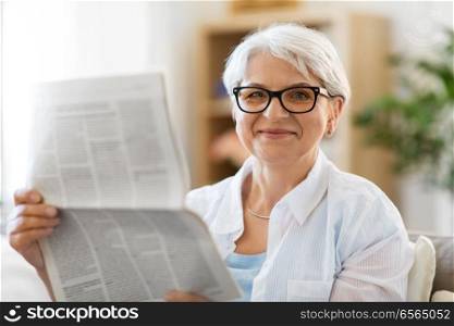 age and people concept - portrait of happy senior woman reading newspaper at home. portrait of senior woman reading newspaper at home