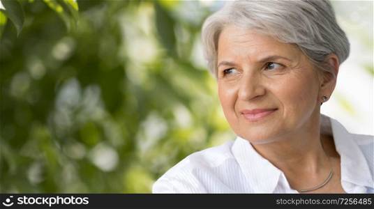 age and people concept - portrait of smiling senior woman over green natural background. portrait of smiling senior woman