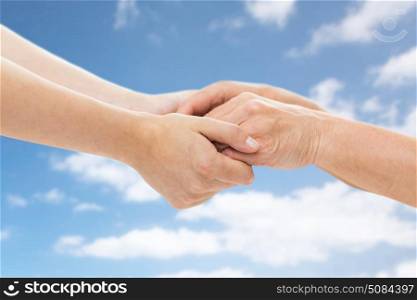 age, care and support concept - close up of senior woman and young woman holding hands over blue sky and clouds background. close up of senior and young woman holding hands. close up of senior and young woman holding hands