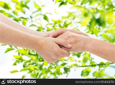 age, care and support concept - close up of senior woman and young woman holding hands over green natural background. close up of senior and young woman holding hands