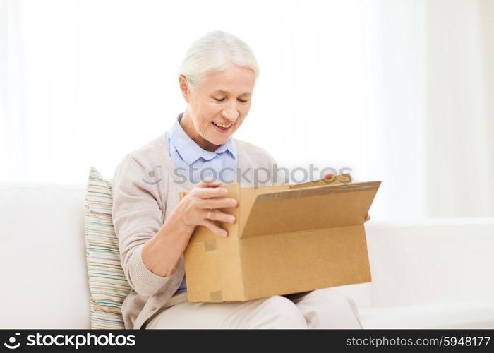 age, delivery, mail, shipping and people concept - happy smiling senior woman looking into open parcel box at home