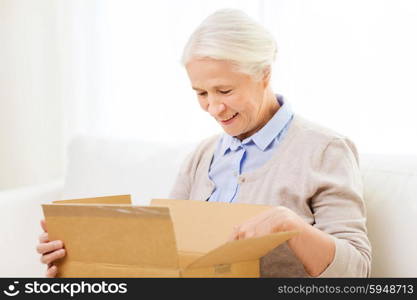 age, delivery, mail, shipping and people concept - happy smiling senior woman looking into open parcel box at home