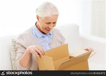 age, delivery, mail, shipping and people concept - happy smiling senior woman looking into open parcel box at home