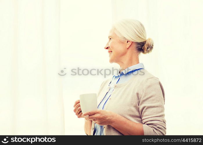 age, drink and people concept - happy smiling senior woman with cup of tea or coffee at home