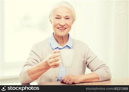 age, drink and people concept - happy smiling senior woman with cup of tea or coffee at home