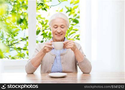age, drink and people concept - happy smiling senior woman with cup of coffee at home over green natural background. happy senior woman with cup of coffee
