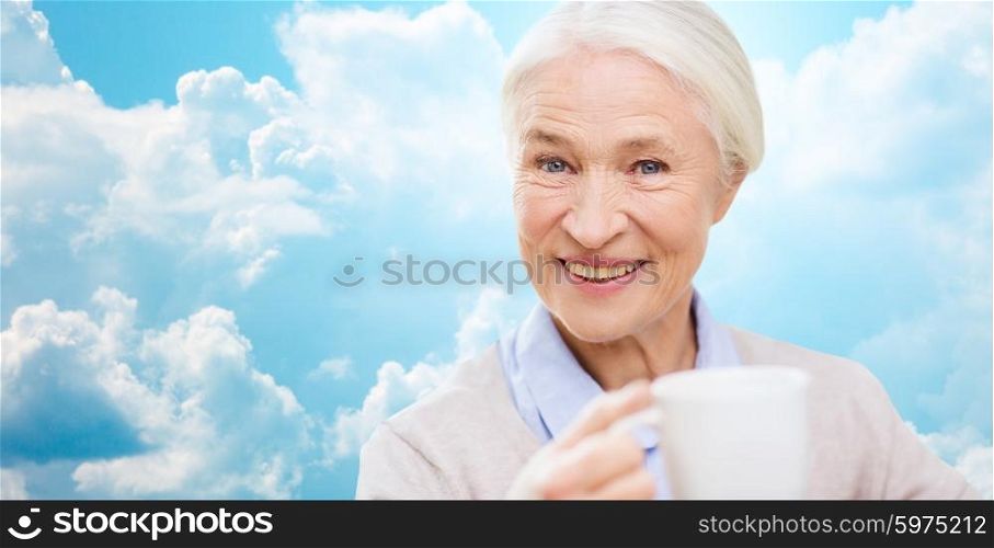 age, drink and people concept - happy smiling senior woman with cup of tea or coffee over blue sky and clouds background