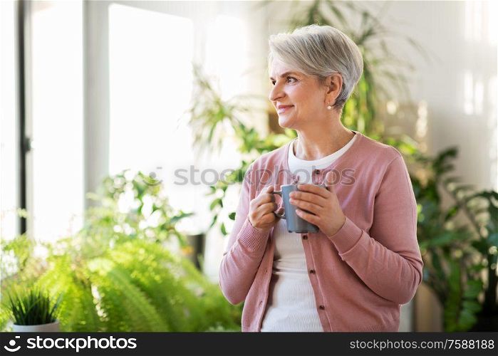 age, drink and people concept - happy smiling senior woman with cup of tea or coffee at home. happy senior woman with cup of tea at home