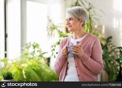 age, drink and people concept - happy smiling senior woman with cup of tea or coffee at home. happy senior woman with cup of tea at home