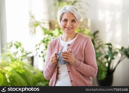 age, drink and people concept - happy smiling senior woman with cup of tea or coffee at home. happy senior woman with cup of tea at home