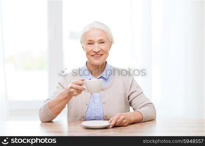 age, drink and people concept - happy smiling senior woman with cup of coffee at home