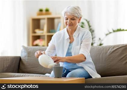 age, drink and people concept - senior woman pouring tea from teapot to cup and drinking it at home. senior woman drinking tea at home