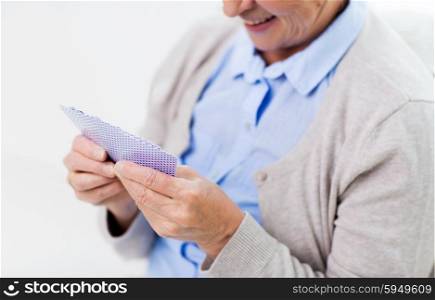 age, game, gamble, poker and people concept - close up of happy smiling senior woman playing cards at home