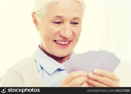age, game, gamble, poker and people concept - happy smiling senior woman playing cards at home