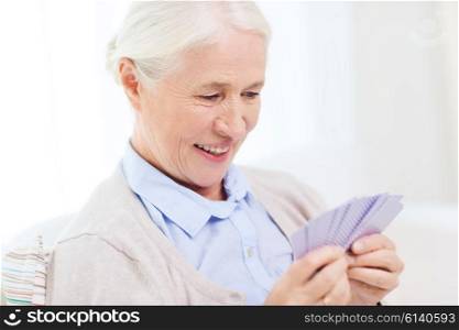 age, game, gamble, poker and people concept - happy smiling senior woman playing cards at home