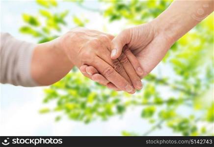 age, generation and care concept - close up of senior woman and young woman holding hands over green natural background. close up of senior and young woman holding hands