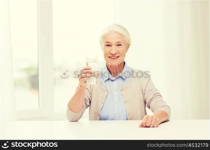 age, health care and people concept - happy senior woman with glass of water at home