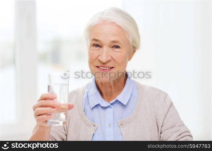 age, health care and people concept - happy senior woman with glass of water at home