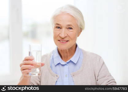 age, health care and people concept - happy senior woman with glass of water at home