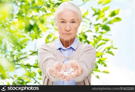 age, healthcare and medicine concept - senior woman with pills over green natural background. senior woman with medicine at home