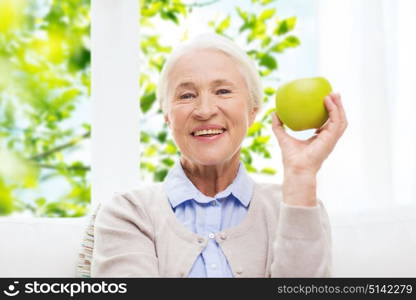 age, healthy eating and people concept - happy smiling senior woman with green apple at home over window and green natural background. happy senior woman with green apple at home