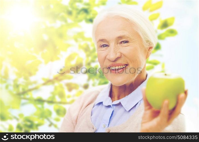 age, healthy eating, food, diet and people concept - happy smiling senior woman with green apple over natural background. happy senior woman with green apple at home. happy senior woman with green apple at home