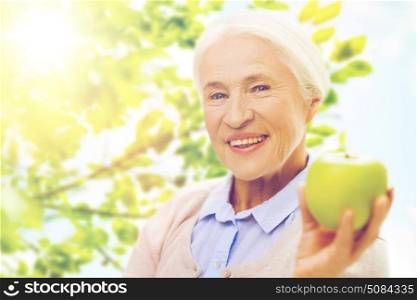 age, healthy eating, food, diet and people concept - happy smiling senior woman with green apple over natural background. happy senior woman with green apple at home. happy senior woman with green apple at home