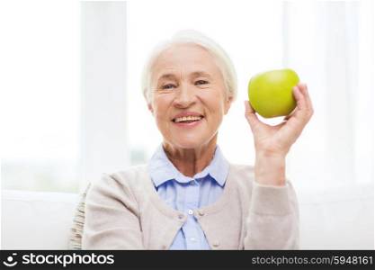 age, healthy eating, food, diet and people concept - happy smiling senior woman with green apple at home