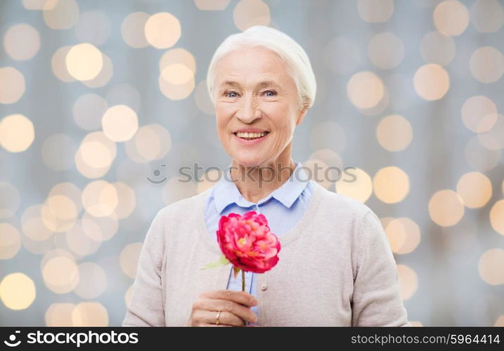 age, holidays and people concept - happy smiling senior woman with flower over holidays lights background