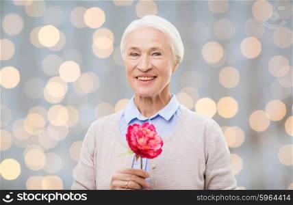 age, holidays and people concept - happy smiling senior woman with flower over holidays lights background