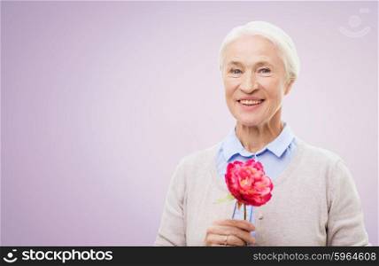 age, holidays and people concept - happy smiling senior woman with flower over violet background