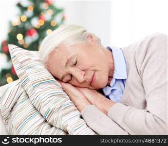age, holidays, relax and people concept - happy senior woman sleeping on pillow at home over christmas tree background
