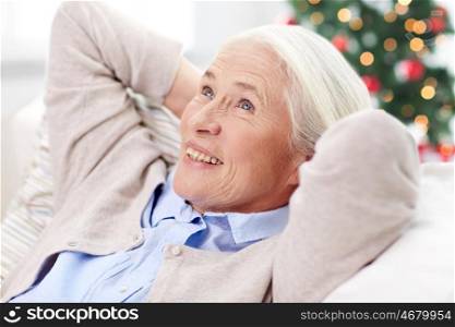 age, holidays, relax and people concept - happy smiling senior woman resting on sofa and dreaming at home over christmas tree background