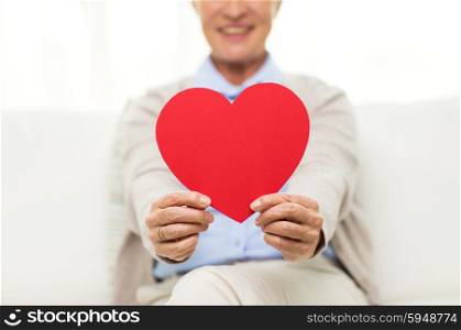age, holidays, valentines day, love and people concept - close up of happy smiling senior woman with red heart shape at home