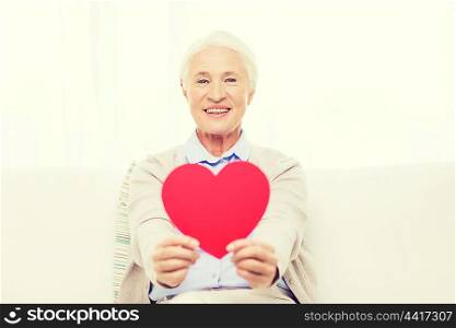 age, holidays, valentines day, love and people concept - happy smiling senior woman with red heart shape at home