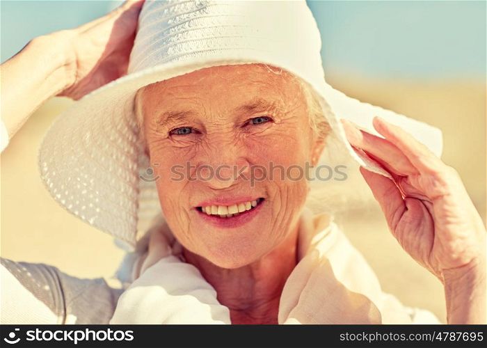 age, leisure and people concept - close up of happy senior woman in sun hat on summer beach